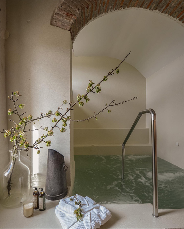 Zona de spa interior con piscina termal, bata blanca, aceites esenciales y decoración natural